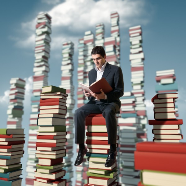 GuyReadingOnStacksOfBooks