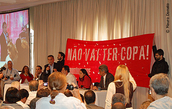 Gilberto Carvalho fala com faixa de protesto ao fundo