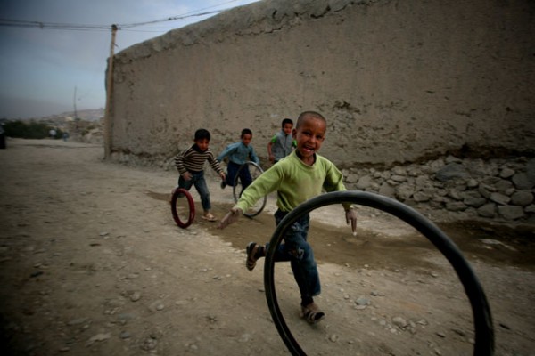 Young Afghan boys run along with bicycle tires at an impoverished loc