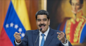 O presidente Nicolás Maduro, da Venezuela, sorrindo ao discursar. Atrás dele, a bandeira da Venezuela e um quadro de Simón Bolívar.