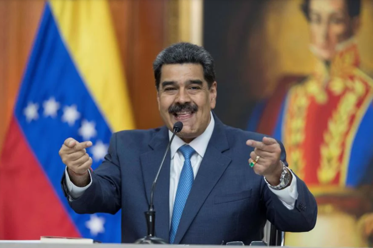 O presidente Nicolás Maduro, da Venezuela, sorrindo ao discursar. Atrás dele, a bandeira da Venezuela e um quadro de Simón Bolívar.
