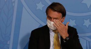 Bolsonaro com máscara e limpando o olho