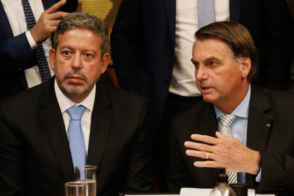 Arthur Lira sentado e Bolsonaro, ao seu lado, olhando