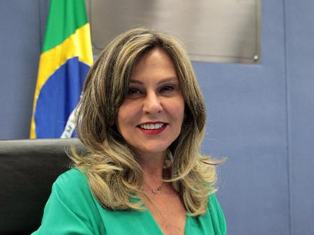 Lindôra Araújo posa para foto com a bandeira do Brasil ao fundo