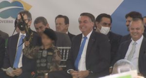Jair Bolsonaro ao lado de criança fardada com arma de brinquedo