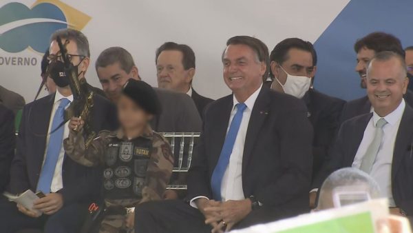 Jair Bolsonaro ao lado de criança fardada com arma de brinquedo