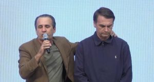 Silas Malafaia, com microfone, orando com as mãos nas costas de Jair Bolsonaro