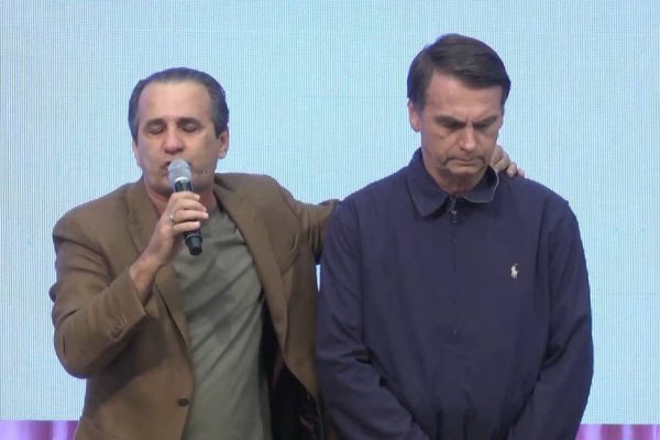 Silas Malafaia, com microfone, orando com as mãos nas costas de Jair Bolsonaro