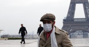 Homem de máscara em frente à Torre Eiffel, na França