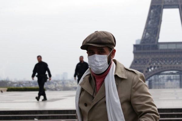 Homem de máscara em frente à Torre Eiffel, na França