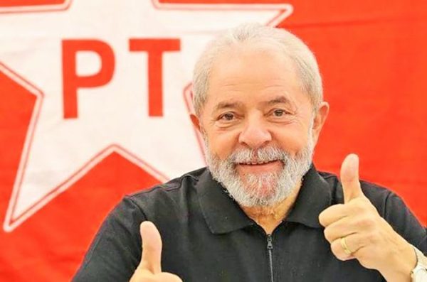 Lula fazendo joinha com o símbolo do PT atrás