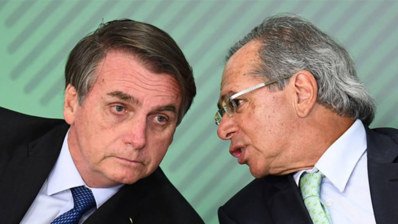 Paulo Guedes falando no ouvido de Bolsonaro, presidente do Brasil