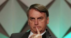 Bolsonaro, sentado e com o dedo na boca, sério