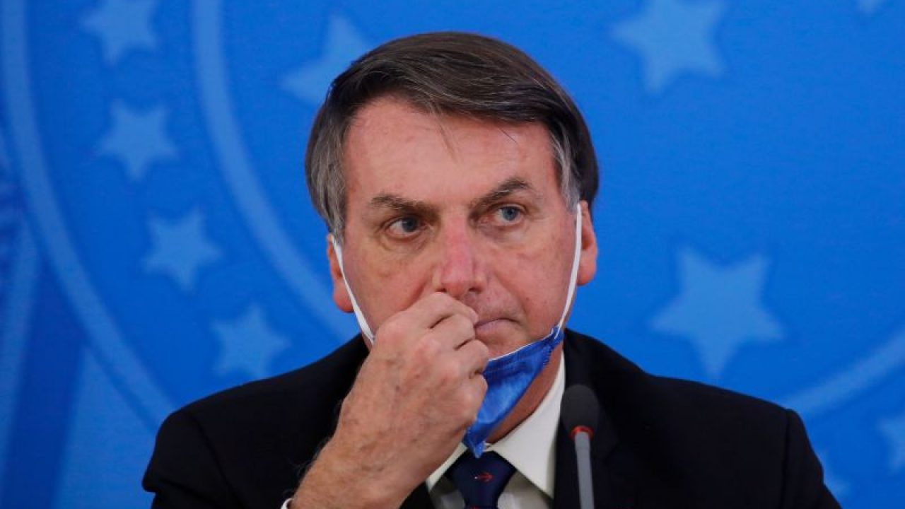 Foto de Bolsonaro com máscara no queixo, olhar pensativo e mão direita na boca.