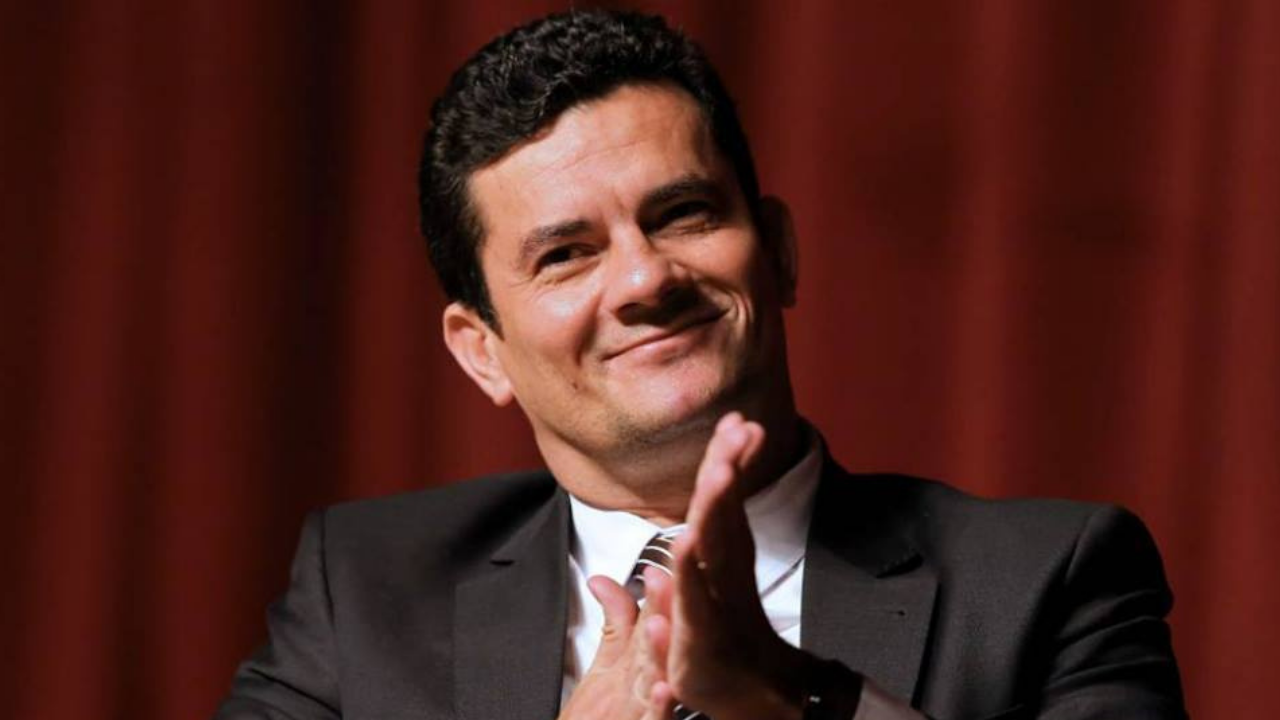 Foto de Sérgio Moro sorrindo, batendo palmas, fundovermelho desfocado
