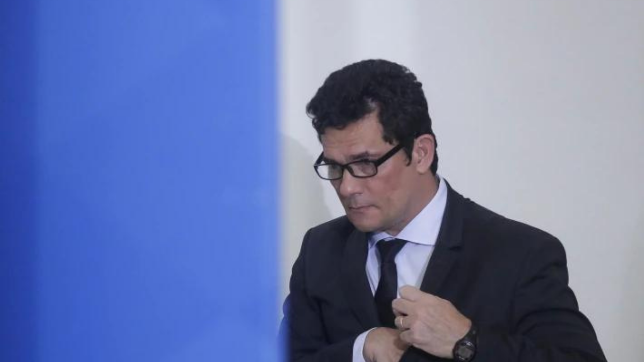 Foto de Sergio Moro distante, ele está com a cabeça abaixada, usando óculos e terno.