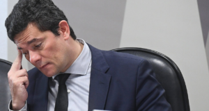 foto de Sergio Moro com olhar preocupado. Cabeça abaixada, franzindo a testa com a mão direita na cabeça.