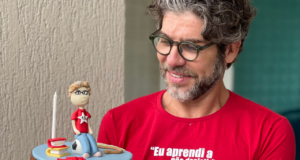 Foto de Juninho Pernambucano com camisa vermelha e bolo com boneco de Lula. Ele tem cabelo e barba grisalhos.