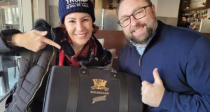 Carla Zambelli usando gorro com o nome Trump e segurando presente para Jason Miller, que está à direita. Ele é branco, tem arba, usa óculos e está com um casaco azul