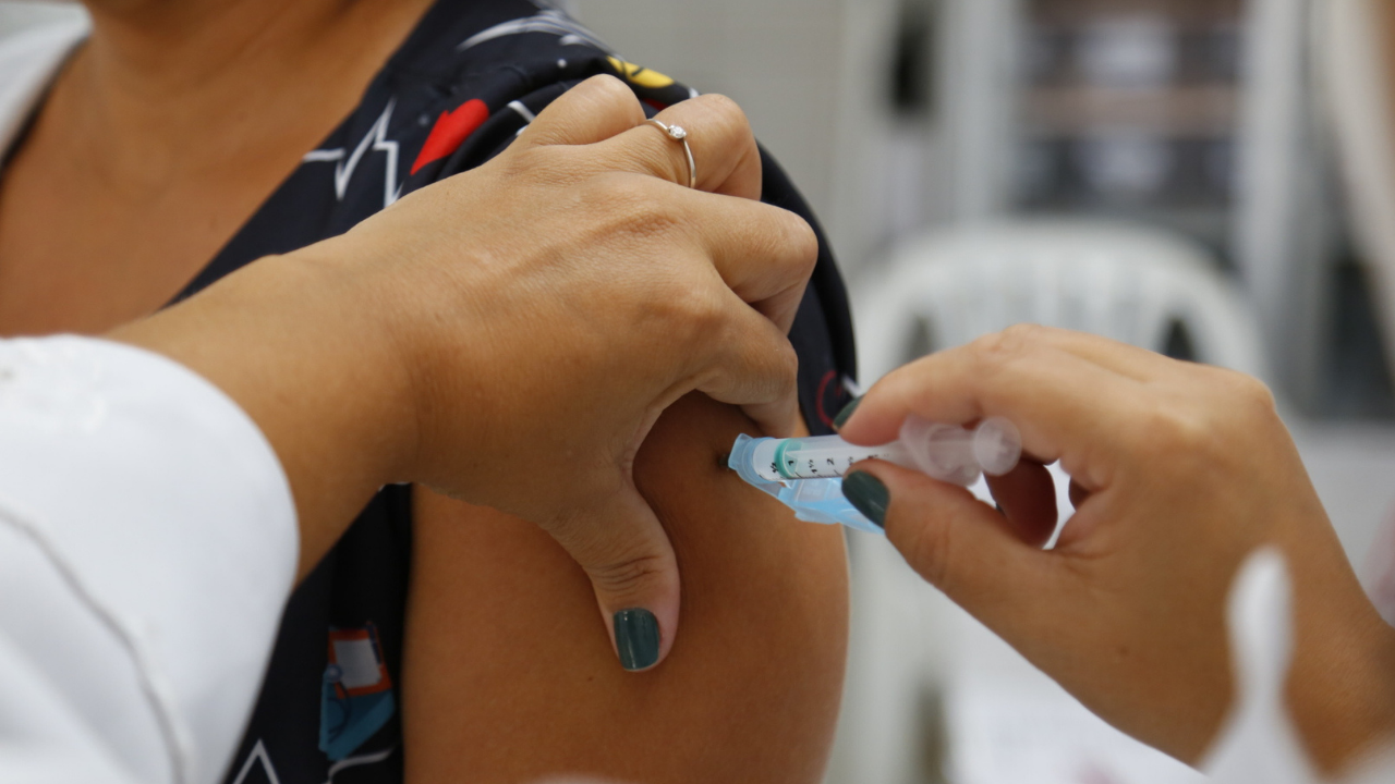 foto de uma pessoa de pele negra recebendo a vacina contra a covid. Na foto, há apenas a imagem do braço direito e uma seringa.