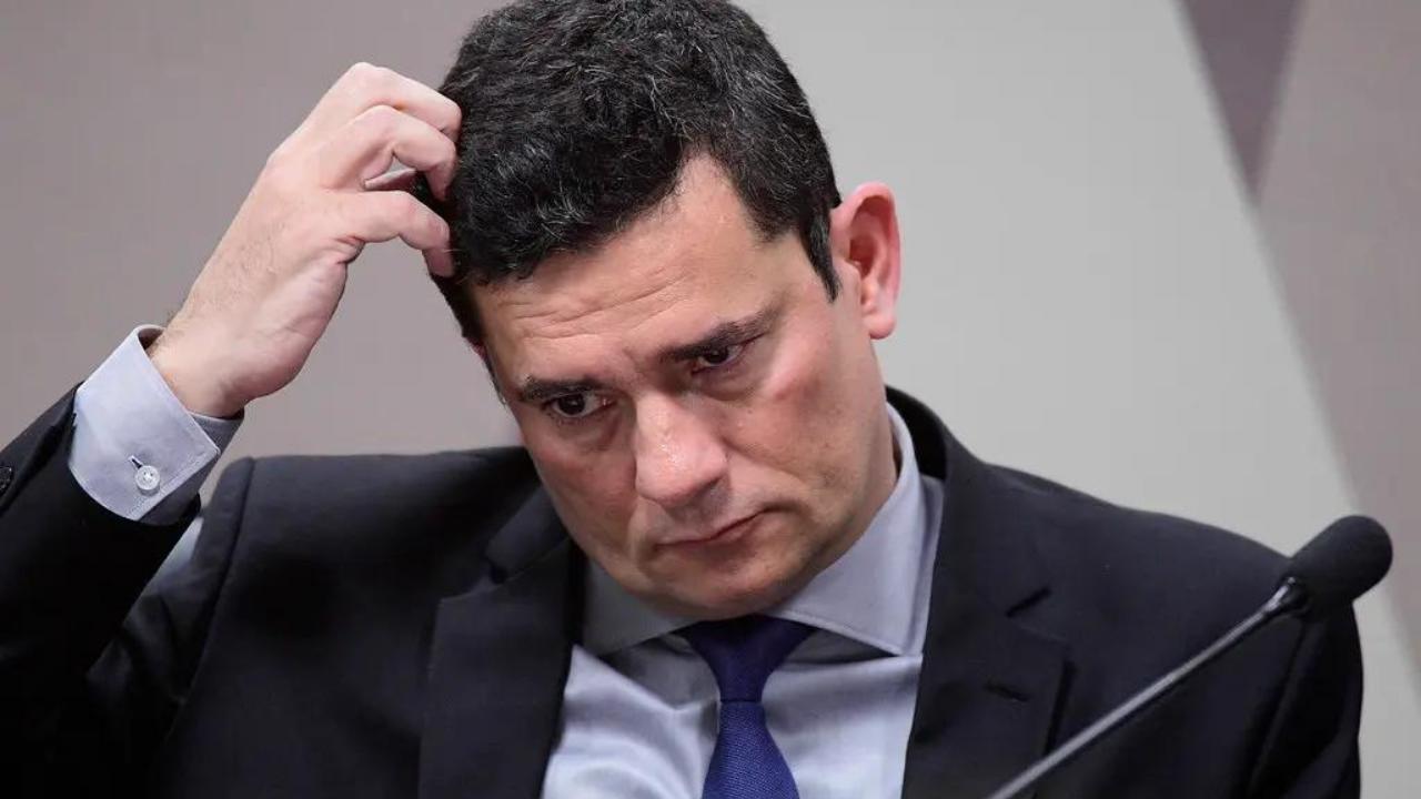 Foto de Sergio Moro com a cabeça baixa, olhar preocupado e mão direita coçando o cabelo na lateral.