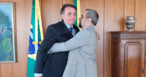 Bolsonaro e Weintraub em um abraço desconcertado no Palácio do Planalto. Ao fundo há bandeiras do país.