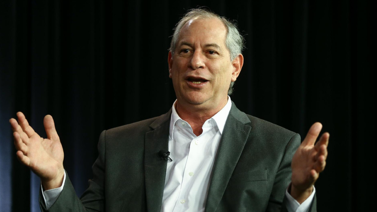 Foto de Ciro Gomes com cara de surpresa, os braços formam um angulo de 90° e ele usa um terno cinza.