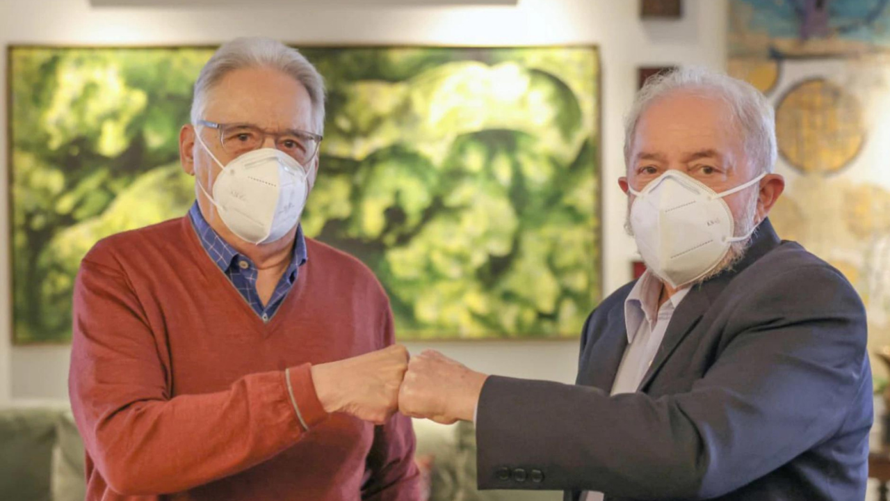 Foto de Lula e FHC cumprimentando-se com os punhos cerrados. Eles usam máscara e olham de forma séria para a câmera.