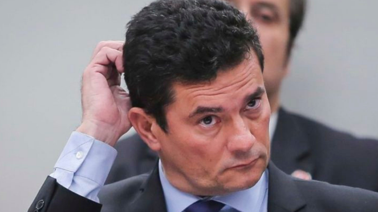 Foto de Sérgio Moro usando terno e com a mão direita levantada atrás da cabeça. Ele tem olhar preocupado.