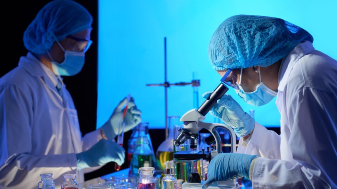 foto de cientistas em laboratório. Há microscópios e eles usam roupas de proteção.