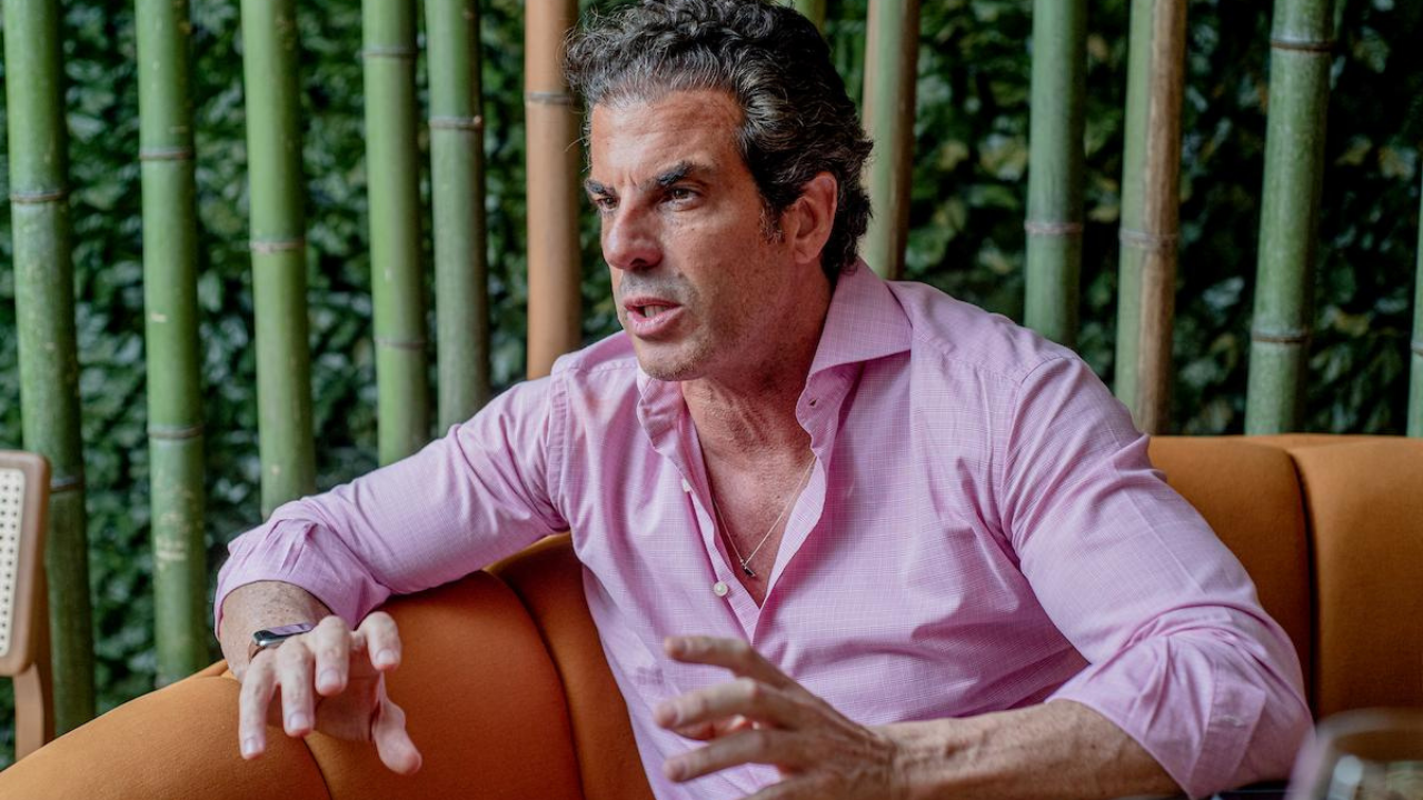 Foto de Álvaro Arcangeli vestindo camisa rosa, gesticulando com as mãos. Ele está sério e tem cabelo grisalho.