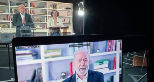 Foto de Lula em uma transmissão ao vivo. Ele está ao lado de Gleisi Hoffmann, presidenta do PT