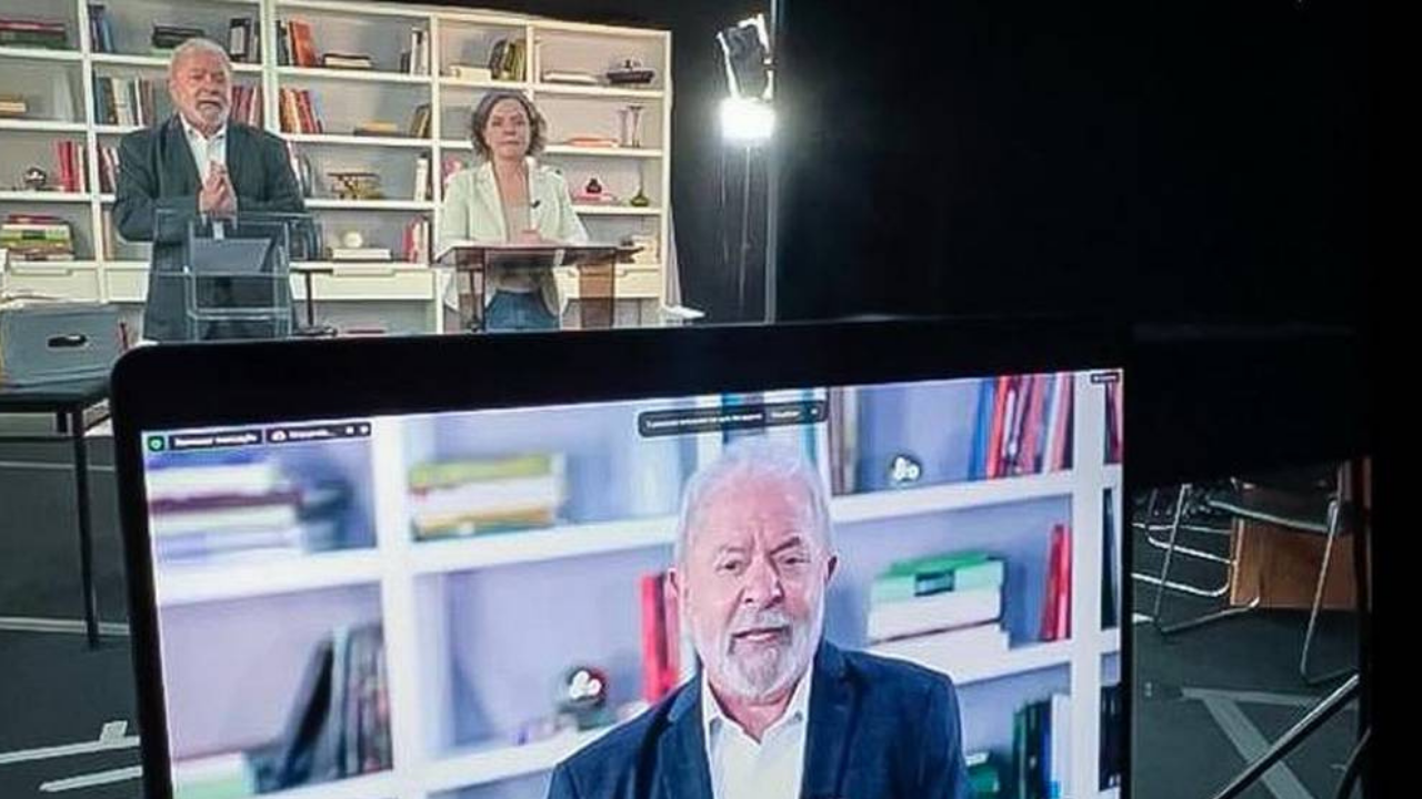 Foto de Lula em uma transmissão ao vivo. Ele está ao lado de Gleisi Hoffmann, presidenta do PT
