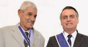 Foto de Bolsonaro (à direita) e Ferraz (à esquerda). Bolsonaro usa um terno preto e Ferraz, cujo apelido é Jacaré, usa uma farda do Exército.