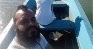 Foto de Cossellu em um barco. Ele usa barba, cabelo preto e uma camisa branca. Ele faz uma selfie.