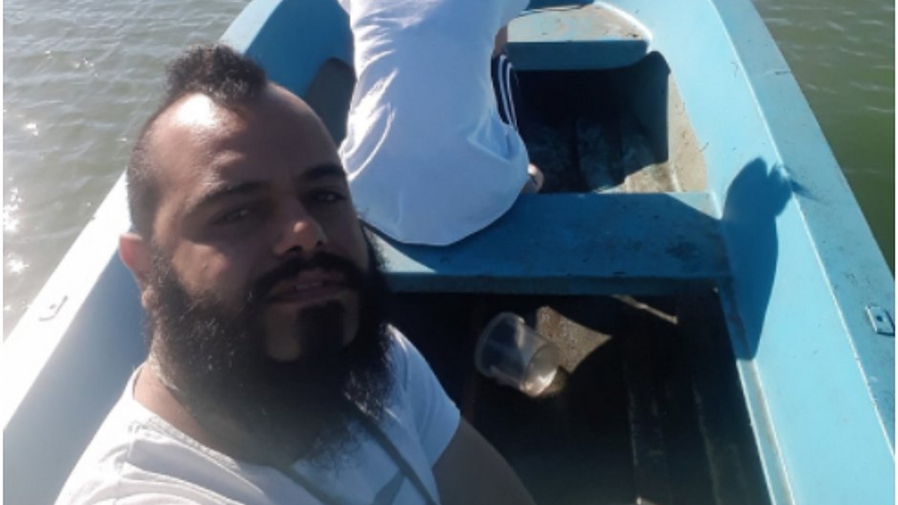 Foto de Cossellu em um barco. Ele usa barba, cabelo preto e uma camisa branca. Ele faz uma selfie.