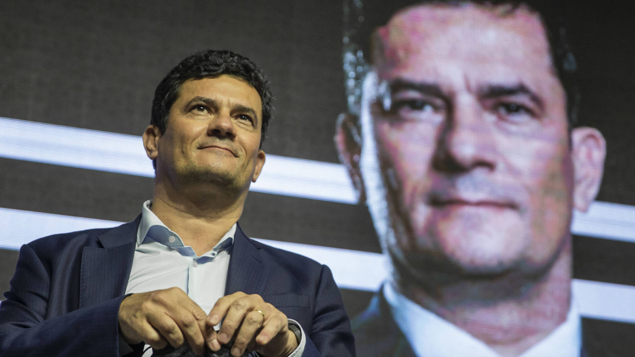 Foto do ex-juiz Sérgio Moro com olhar confiante. Ao fundo uma imagem dele de campanha.
