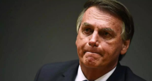 Bolsonaro prendendo os lábios dentro da boca com olhar preocupado. Ele usa um terno preto.