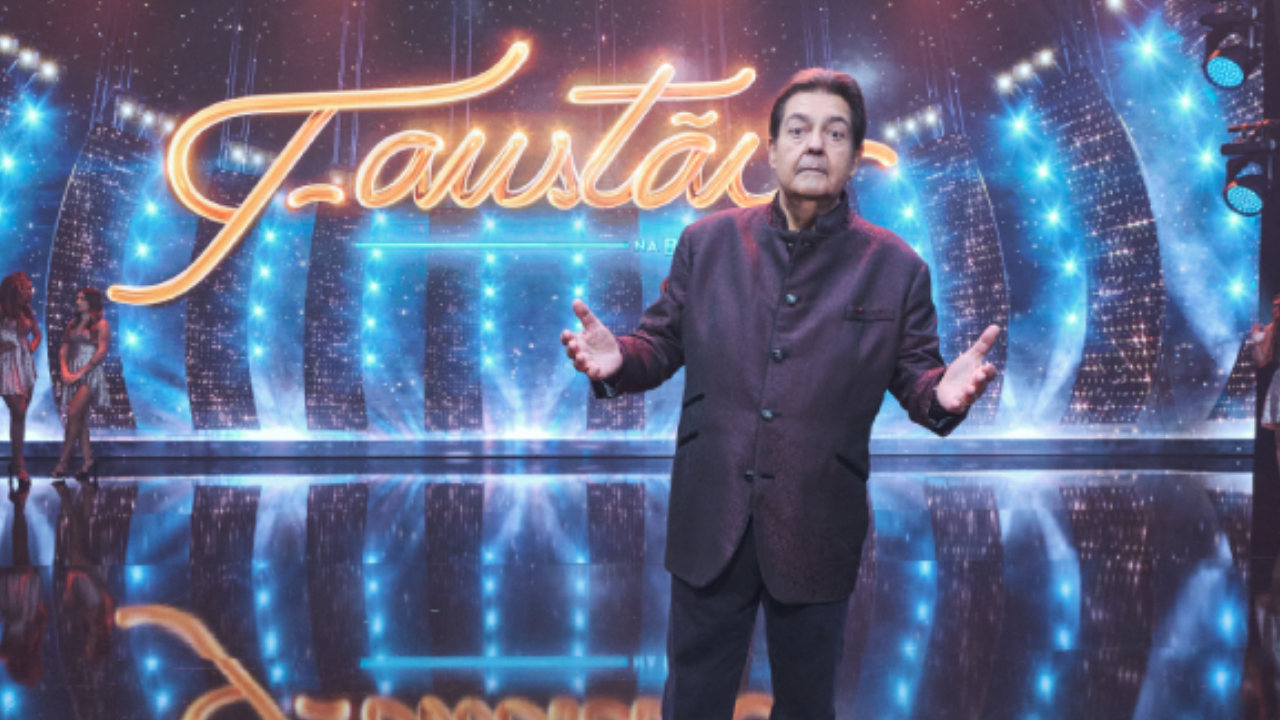 Foto de Faustão com um terno e calça preta. Ao fundo há o estúdio do programa 'Faustão na Band'.