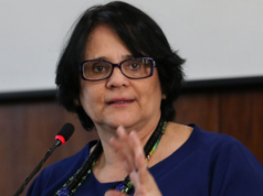 Foto da Ministra Damares Alves falando so microfone. Ela usa uma blusa verde e óculos de grau.