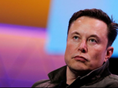 Elon Musk com olhar desatento e cara séria. Ele é branco e usa cabelo preto, fundo colorido desfocado.