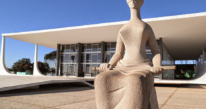 Imagem da frente do prédio do STF, com a estátua da justiça na frente.