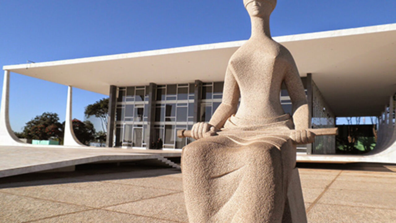 Imagem da frente do prédio do STF, com a estátua da justiça na frente.