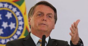 Bolsonaro, com olhar assustado, falando ao microfone. Ele usa terno preto.