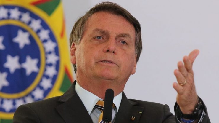 Bolsonaro, com olhar assustado, falando ao microfone. Ele usa terno preto.