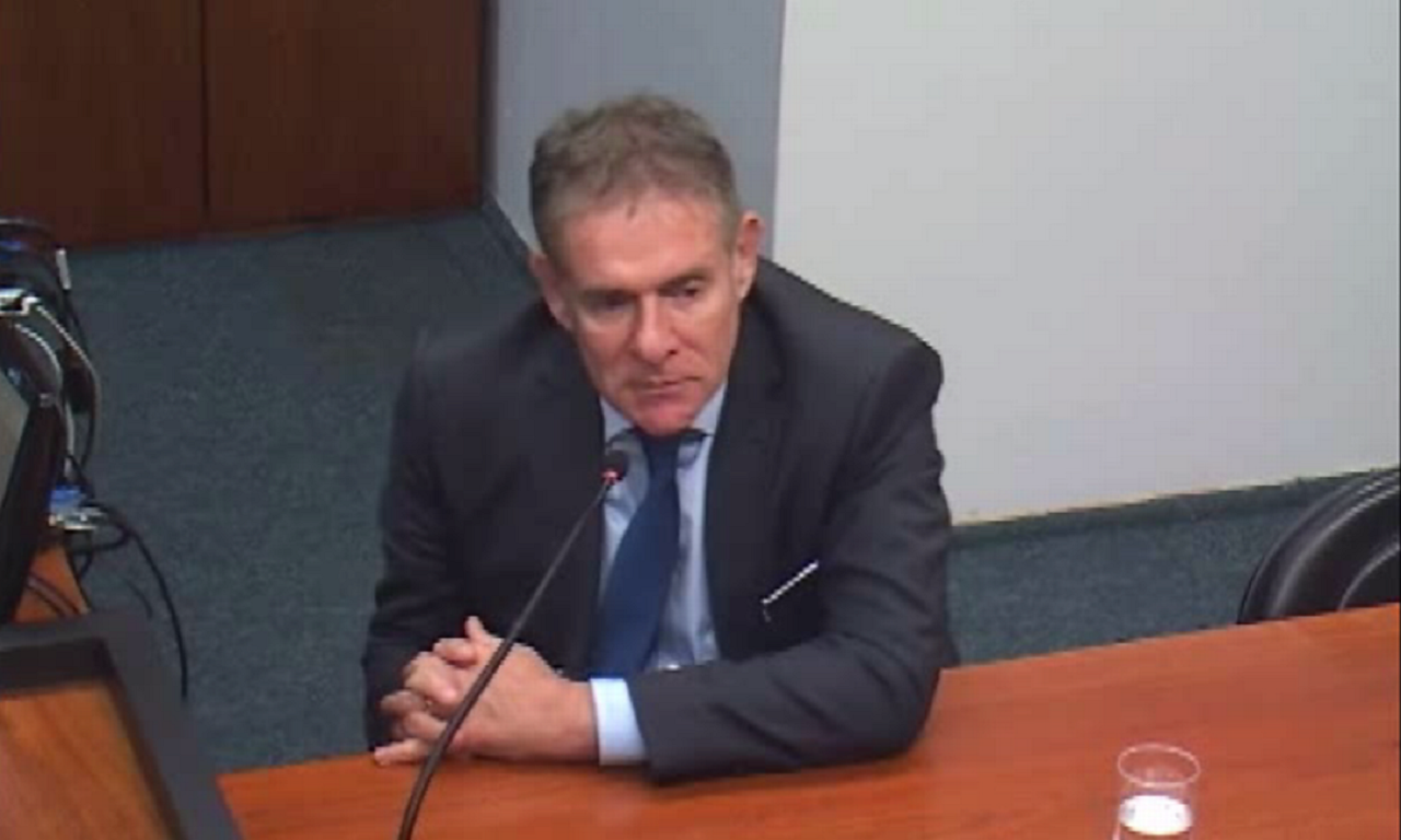 Roberto Bertholdo sentado, com um microfone numa mesa, em sua frente