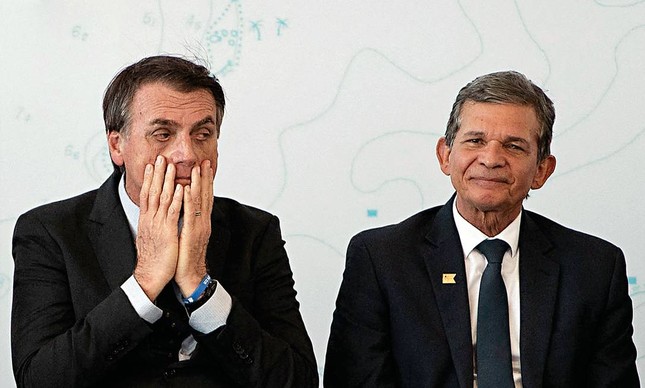 Bolsonaro com a mão no rosto e expressão de cansado ao lado de Joaquim Silva e Luna, presidente da Petrobras, que sorri de forma modesta.