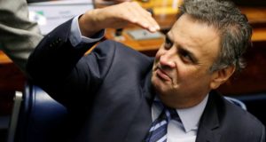 Aécio Neves de terno e gravata sentado em sua cadeira na Câmara dos Deputados.