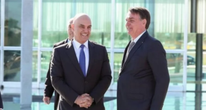 O ministro do STF Alexandre de Moraes ao lado do presidente Jair Bolsonaro (PL), ambos de pé e sorrindo.