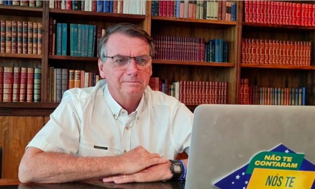 Bolsonaro sentado, de óculos, olhando para notebook, dando entrevista de forma remota.